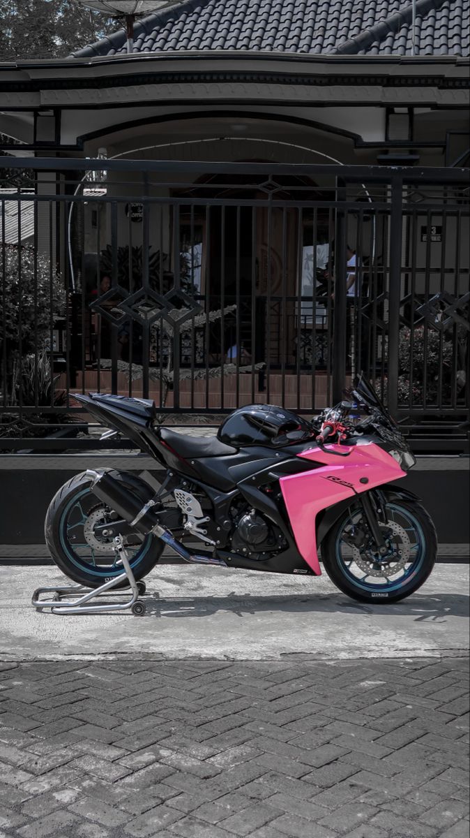 a pink and black motorcycle parked in front of a gated area with iron railings