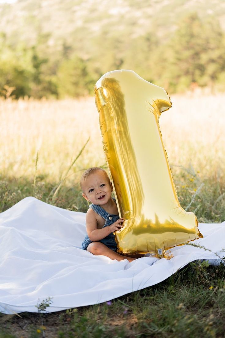 a baby sitting on a blanket with a large balloon in the shape of a number one