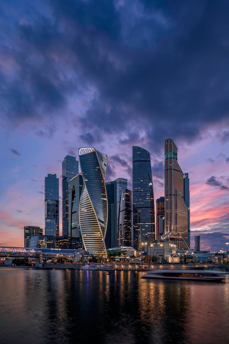 the city skyline is lit up at night with boats in the water and skyscrapers on either side