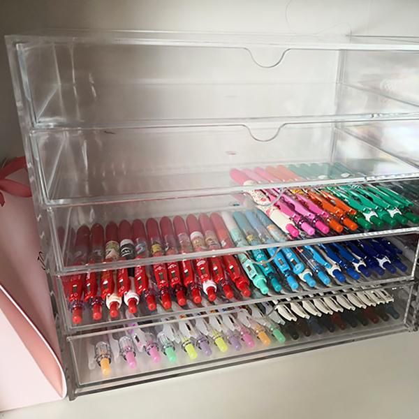 a clear plastic drawer filled with lots of different colored pens and pencils on top of a white table