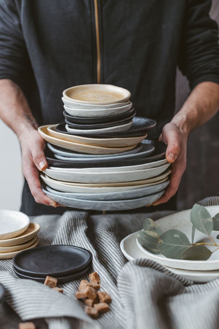 a man holding a stack of plates on top of a table next to other dishes