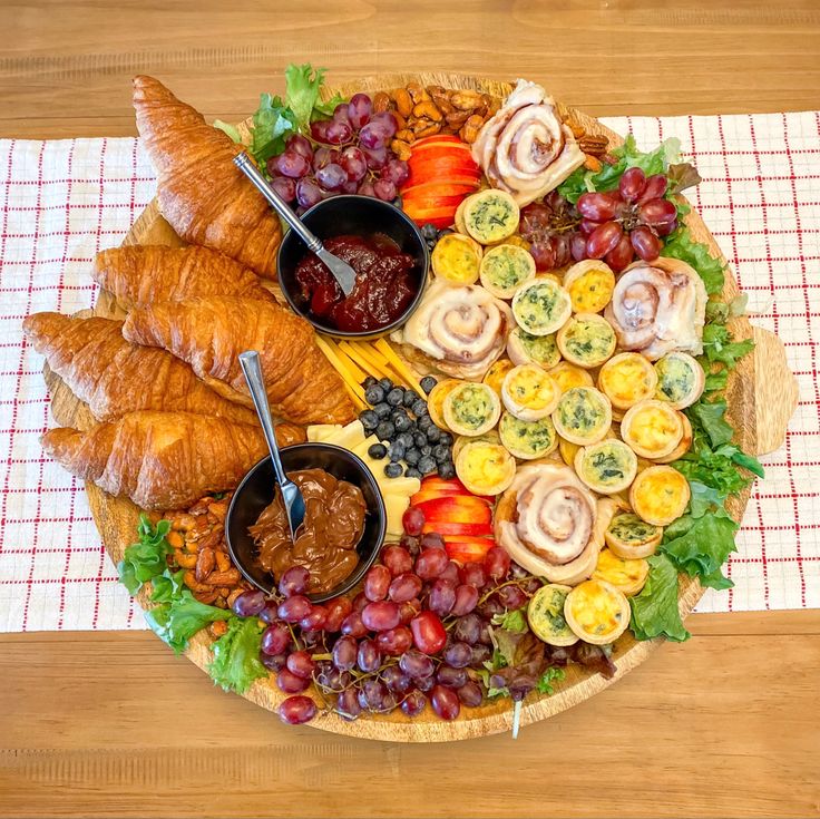 a platter filled with croissants, grapes, bread and other foods