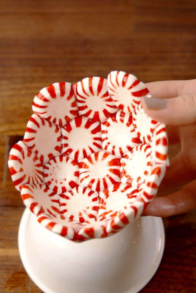 a hand holding a red and white bowl on top of a wooden table next to a cup filled with candy canes