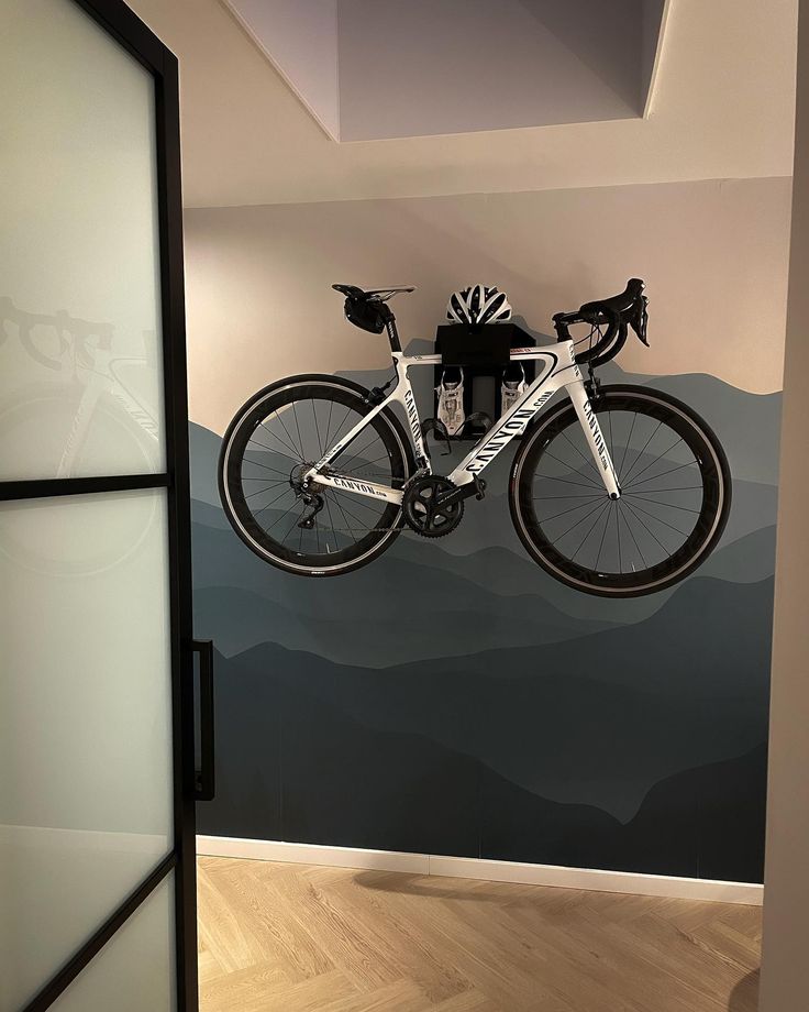 a bike hanging from the ceiling in a room with mountains painted on the wall behind it