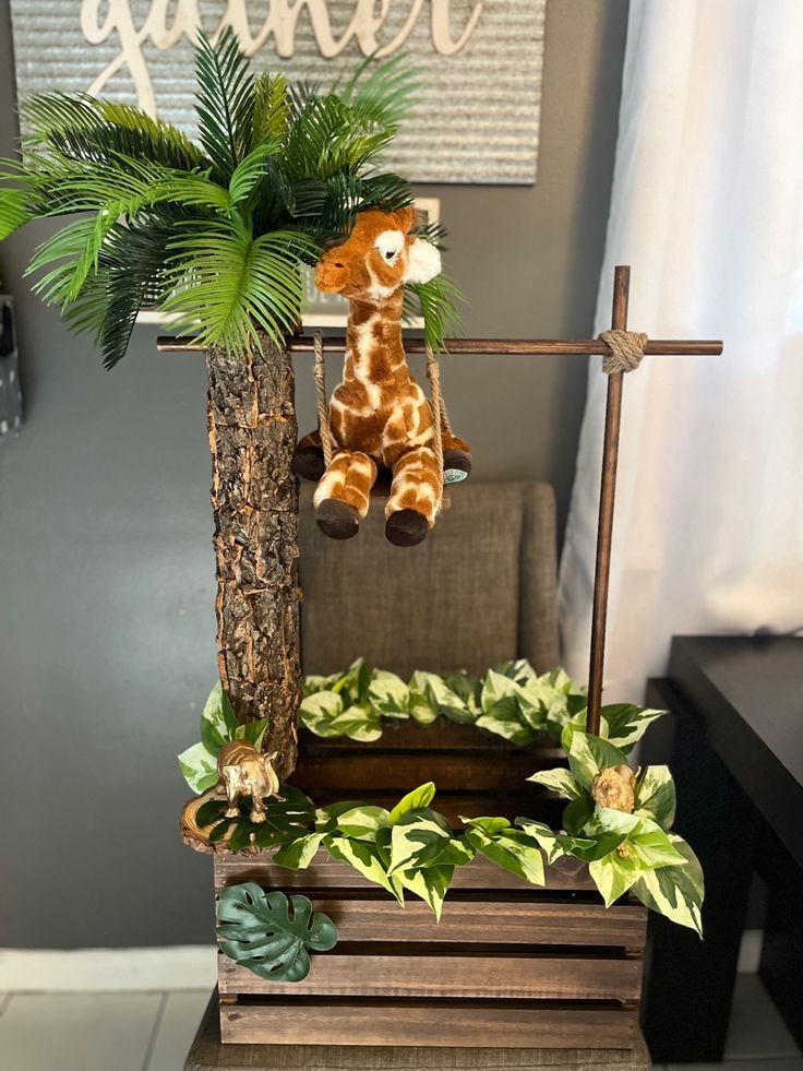 a stuffed giraffe hanging from a cross on top of a wooden crate with greenery