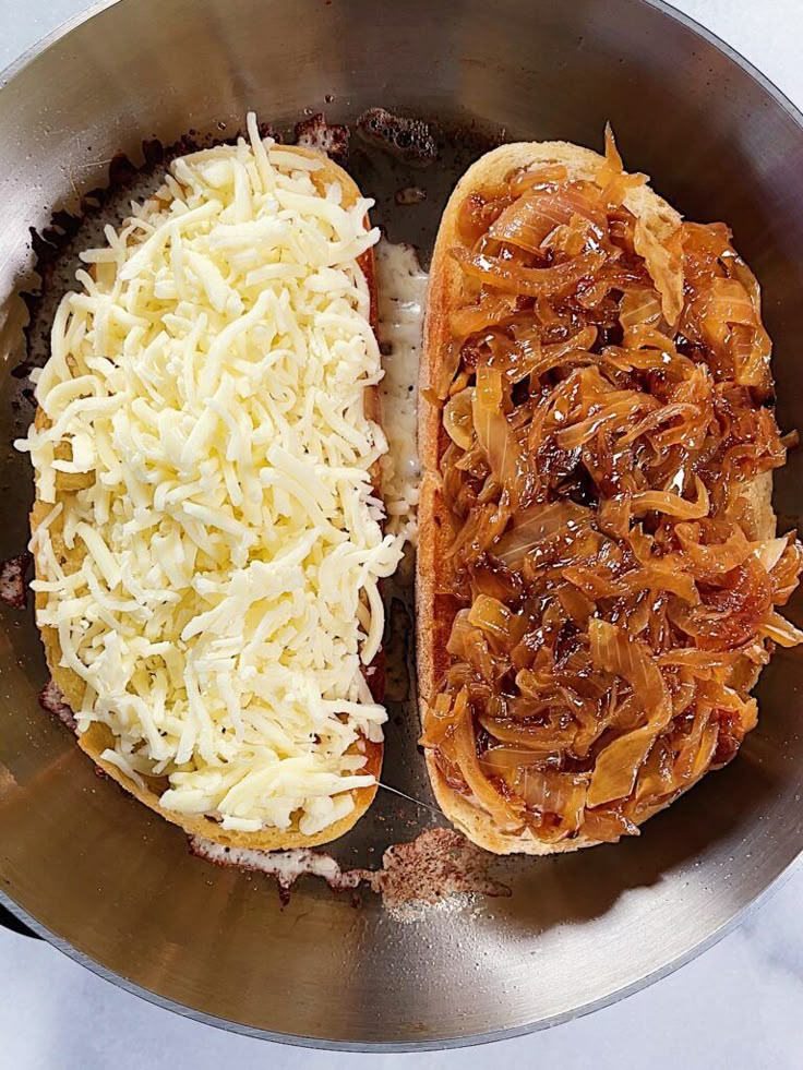 two hot dogs with onions and cheese in a metal pan on a counter top, ready to be eaten