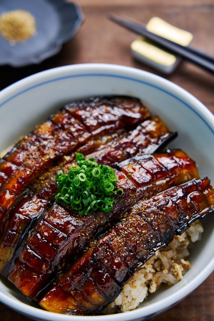 a bowl filled with meat and rice on top of a wooden table next to chopsticks