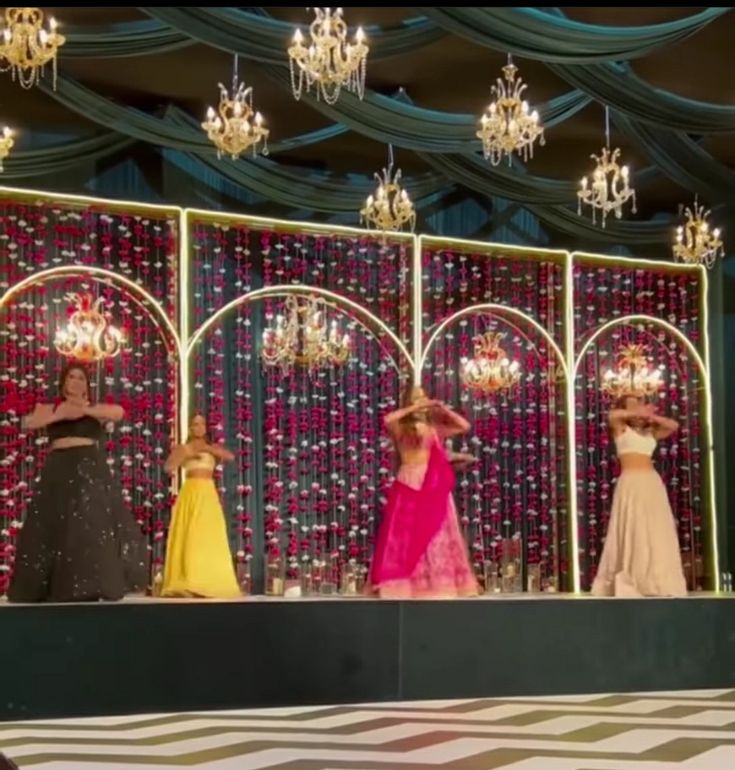 three mannequins dressed in dresses and hats on stage with chandeliers