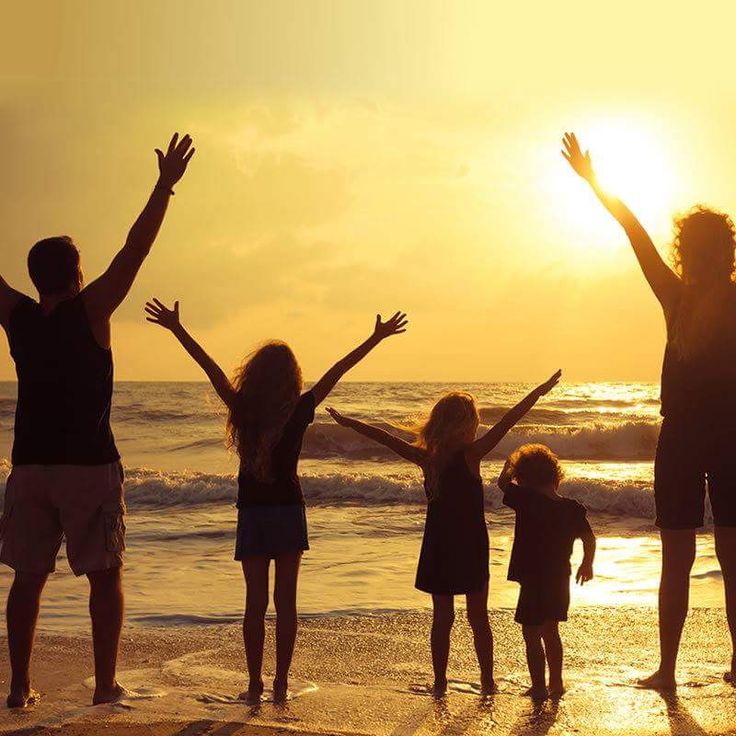 a group of people standing on top of a beach next to the ocean at sunset