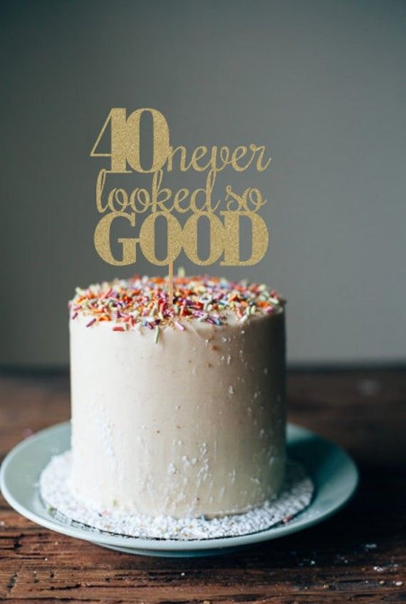 a white cake with gold lettering and sprinkles is on a wooden table