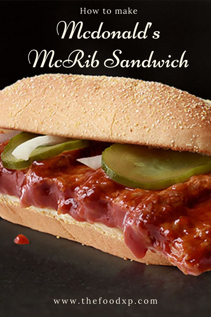 a sandwich with meat, pickles and sauce on it sitting on a black surface