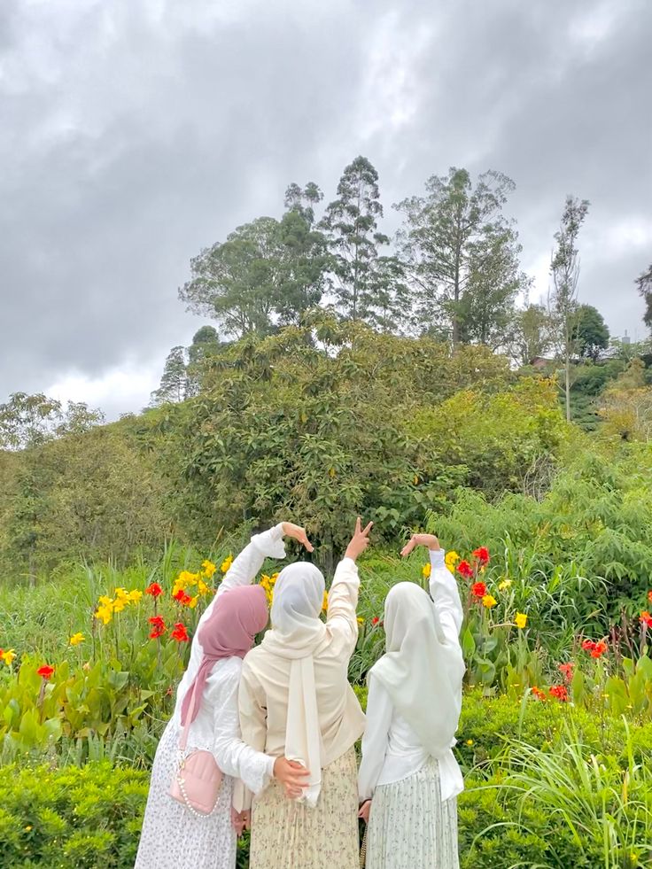 three women standing in front of flowers and trees with their hands up to the sky