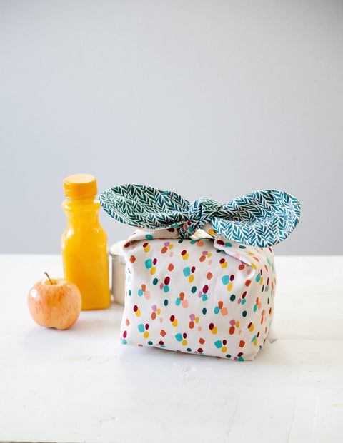 an apple, orange juice and wrapping paper on a table next to some condiments