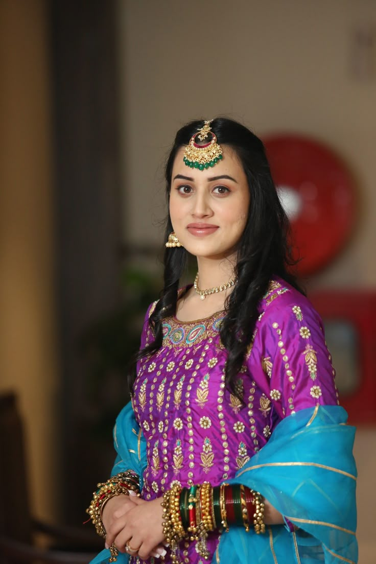 a woman in a purple and blue outfit with gold jewelry on her head, posing for the camera