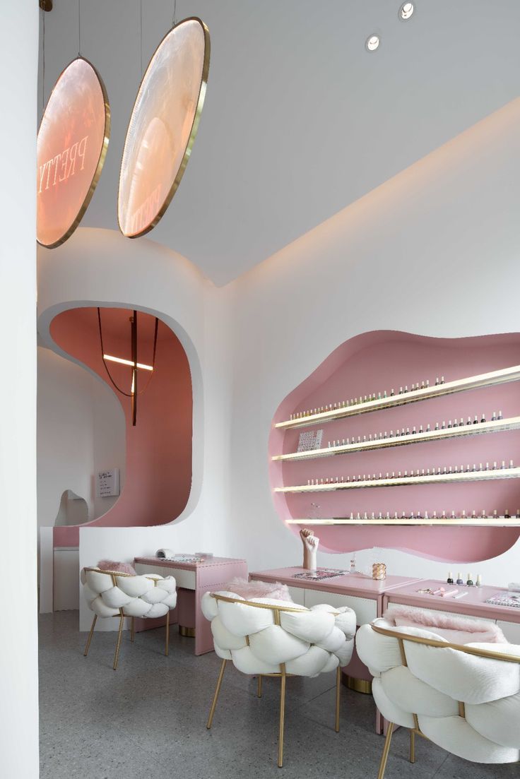 the interior of a salon with pink and white chairs, round lights, and circular mirrors