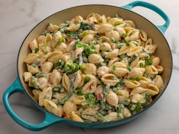 a blue skillet filled with pasta and broccoli on top of a white counter