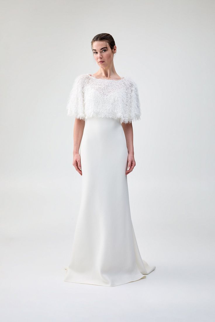 The Pluma Cape is an elegant finishing touch to any bridal gown or wedding look, adorned with a bespoke feather look fabrication. Crafted with a wrap design, this piece falls beautifully around your shoulders, with layers of flowing fabric in alternating lengths and textures. The Pluma Cape is designed to be worn around the shoulders, with four button closures along the back. This is a one-size garment. Wedding Evening Dress With Fitted Bodice And Cape Sleeves, Wedding Evening Dress With Cape Sleeves, White Dress With Cape Sleeves For Reception, Wedding Evening Dress With Feather Trim And Fitted Bodice, Fitted Feather Trim Evening Dress For Wedding, Fitted Evening Dress With Feather Trim For Wedding, Fitted Wedding Evening Dress With Feather Trim, Wedding Dress With Feather Trim And Fitted Bodice, Elegant Feather-trim Wedding Gown