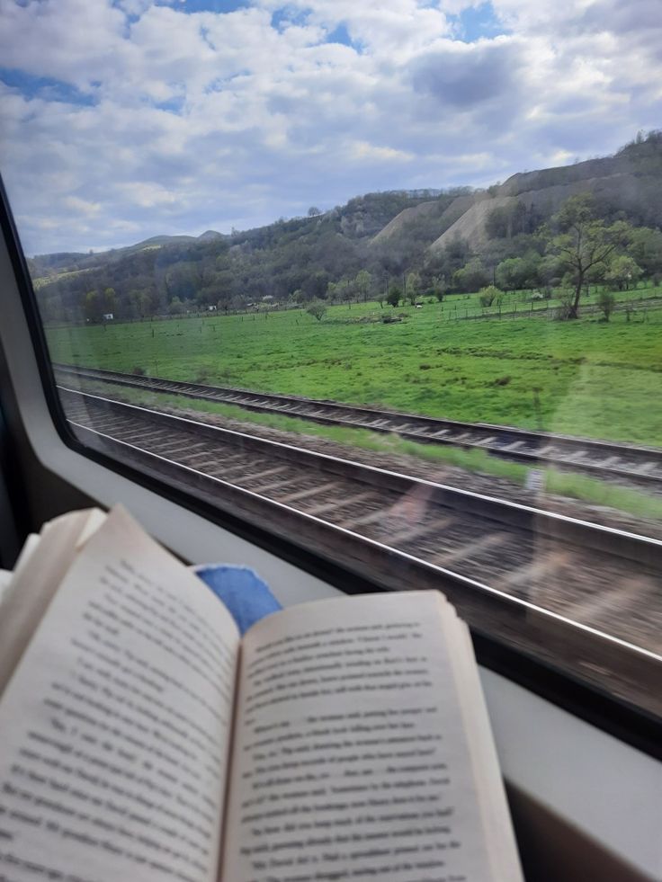 an open book sitting on top of a table next to a window with a view of a field