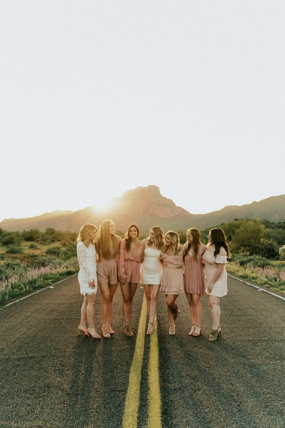 four women standing in the middle of an empty road with mountains in the back ground