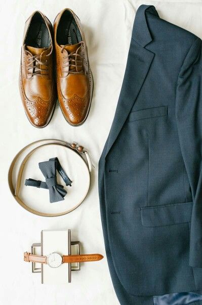 a suit, tie, and shoes are laid out on a white sheet next to a watch