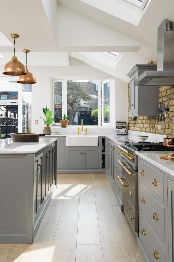 a kitchen with grey cabinets and white counter tops, gold pulls on the handles in front of an open window