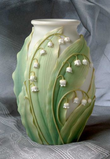 a green and white vase sitting on top of a gray cloth covered tablecloth with lily of the valley design