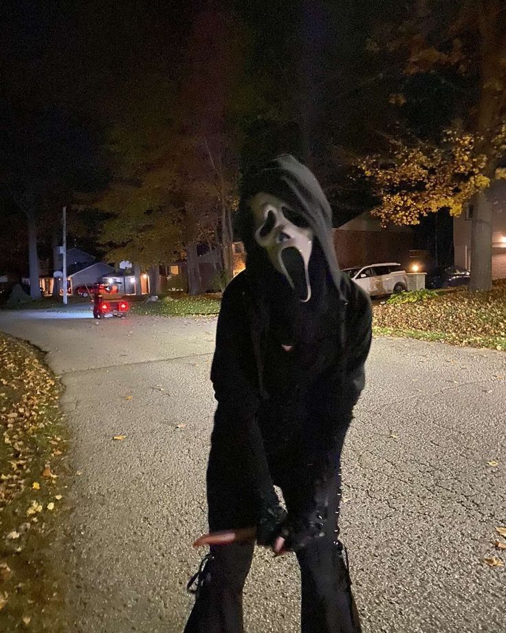 a person wearing a mask and holding a skateboard on a street at night with trees in the background