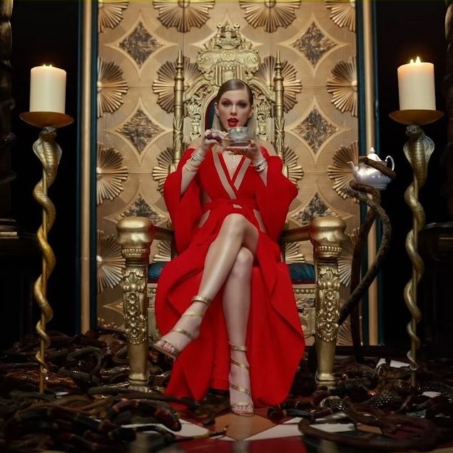 a woman in a red dress is sitting on a throne with candles and a teapot