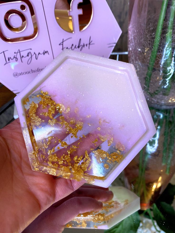 a person holding up a piece of glass with gold flakes on it in front of a vase