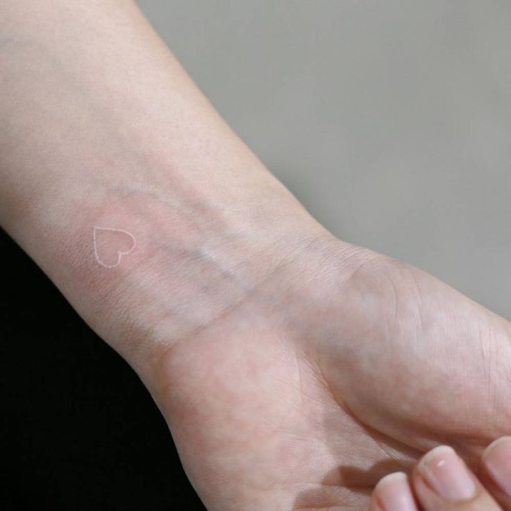 a person's arm with a small white heart tattoo on it