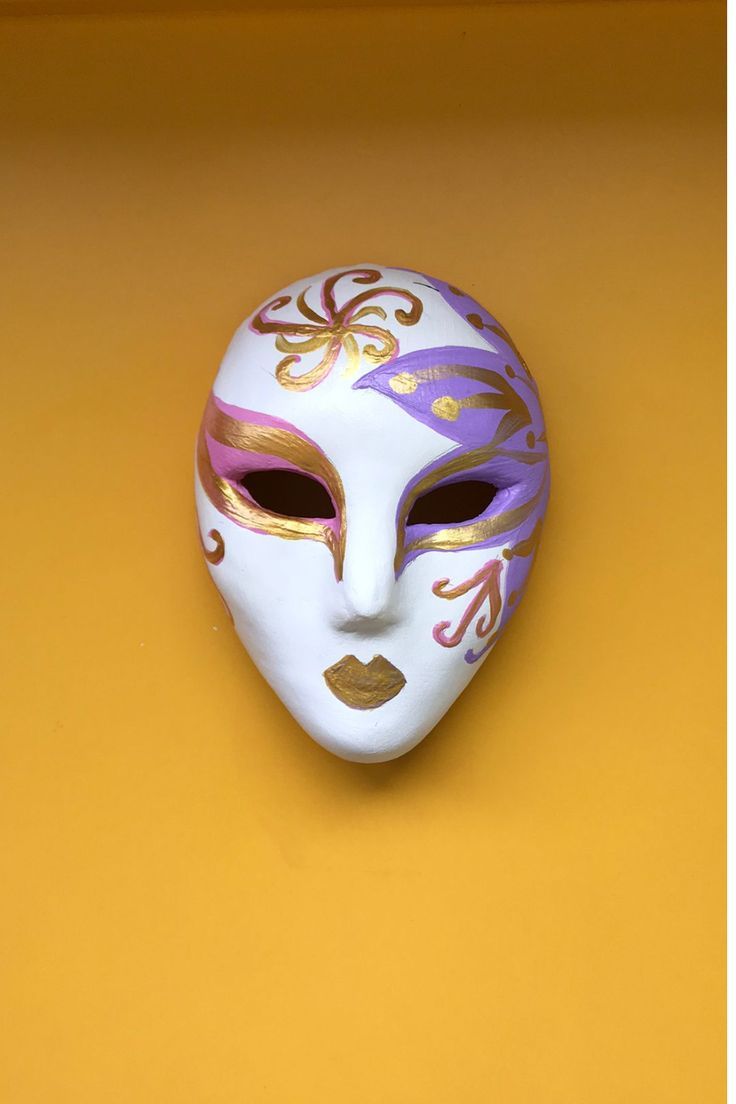 a white mask with purple and gold designs on it sitting on a yellow table top