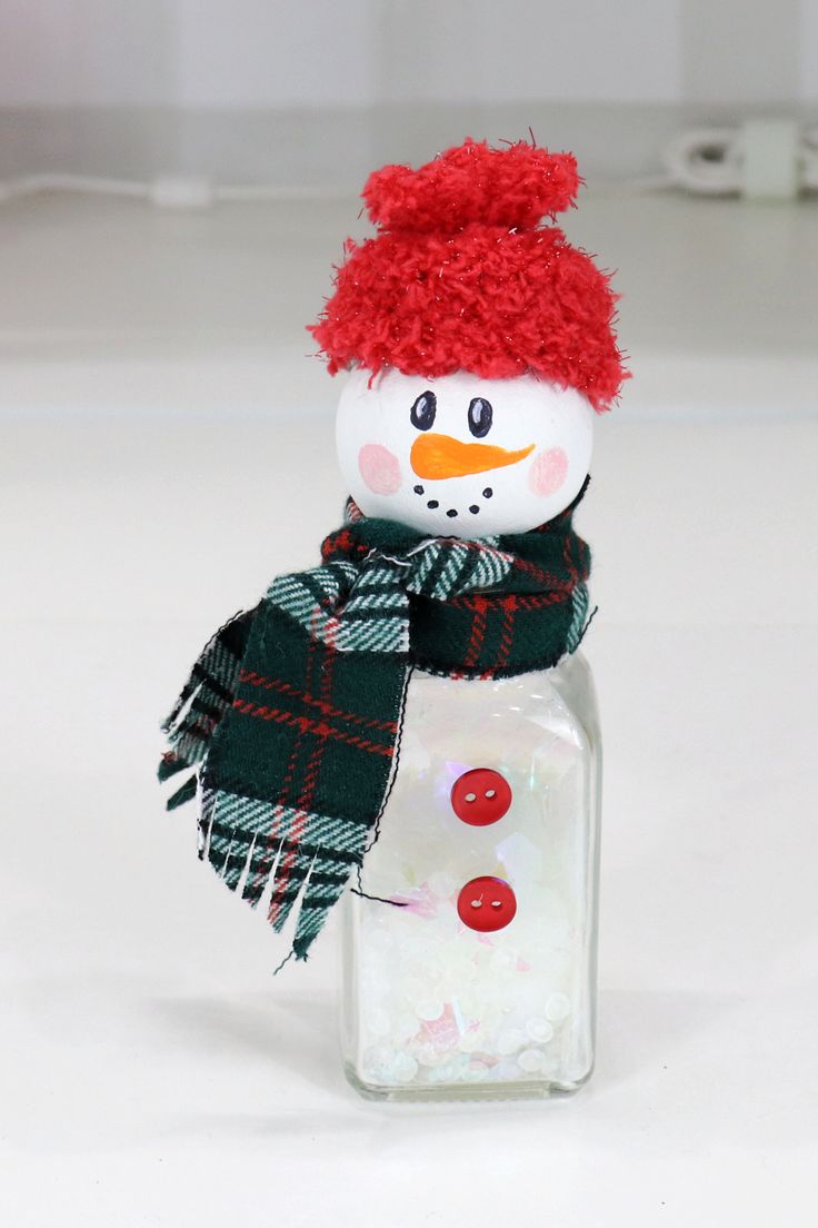 a snowman in a red hat and scarf sitting on top of a glass jar