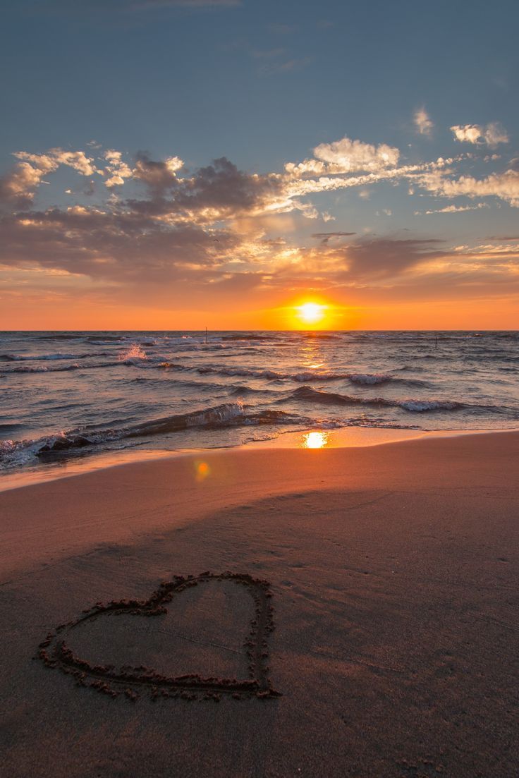 a heart drawn in the sand at sunset