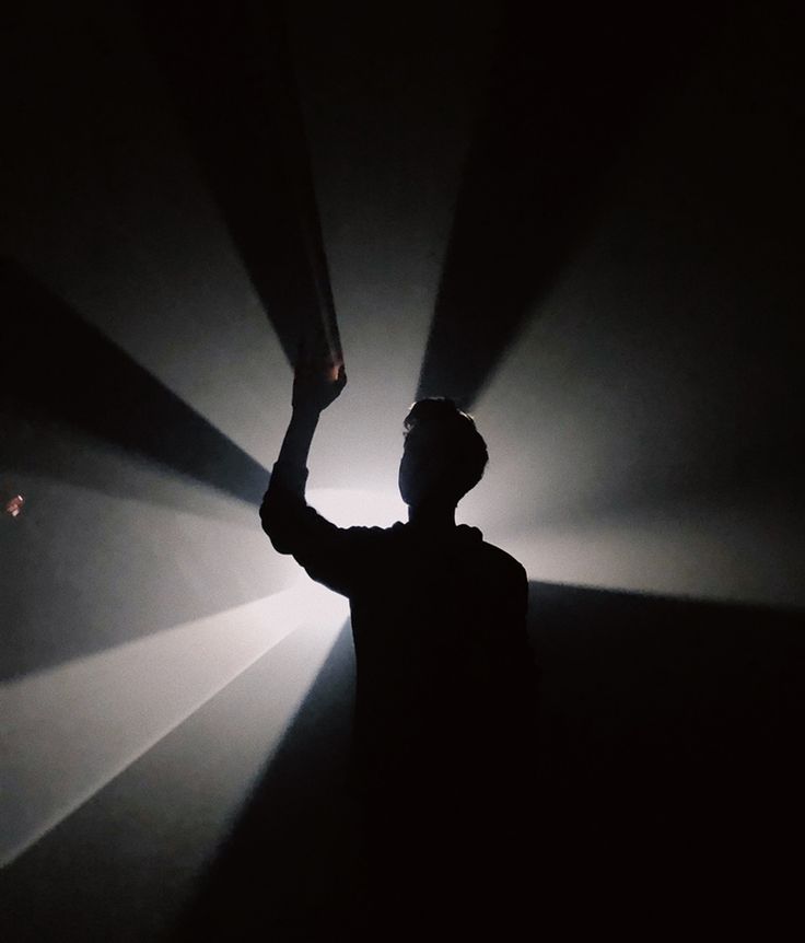 a man standing in the dark with his arm raised up and light shining from behind him