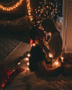 a man and woman sitting on the floor in front of a christmas tree with lights