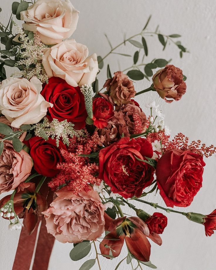 a vase filled with lots of red and pink flowers on top of a white wall