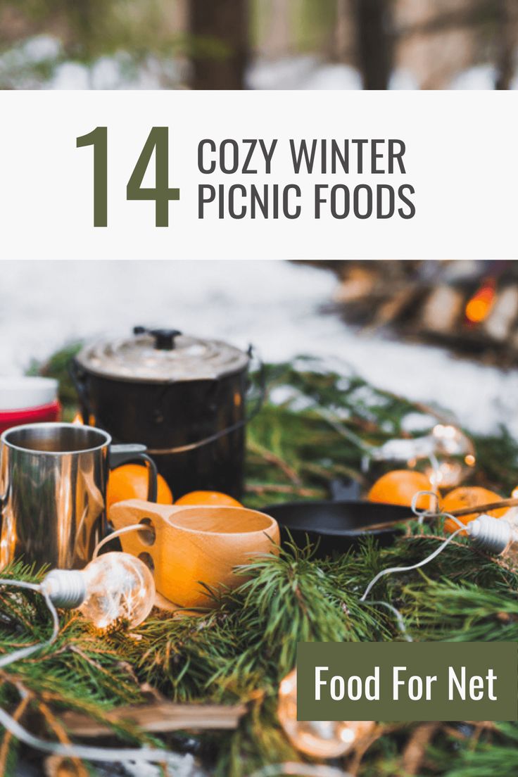 a table topped with lots of food on top of a snow covered ground next to trees