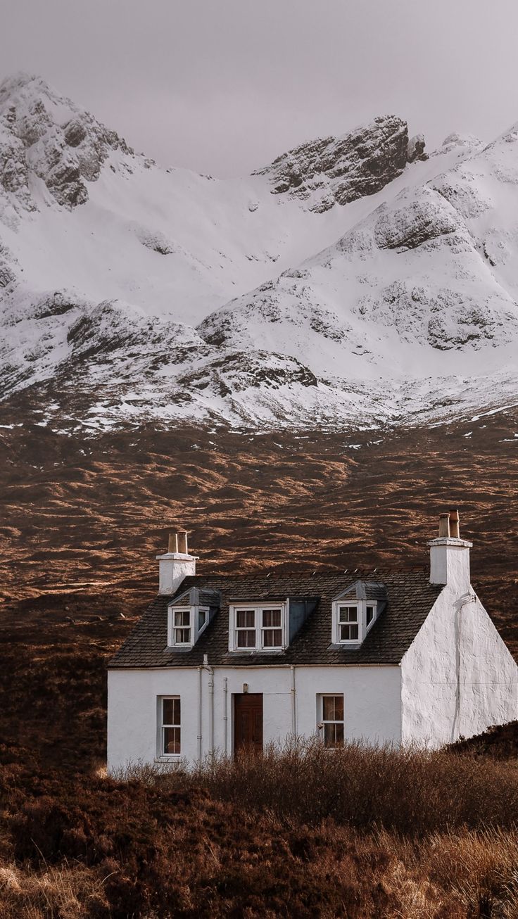 a white house in the middle of a field with mountains in the backgroud