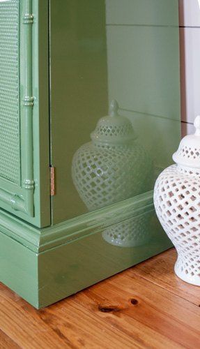 a green cabinet sitting on top of a wooden floor next to a white vase with a lid