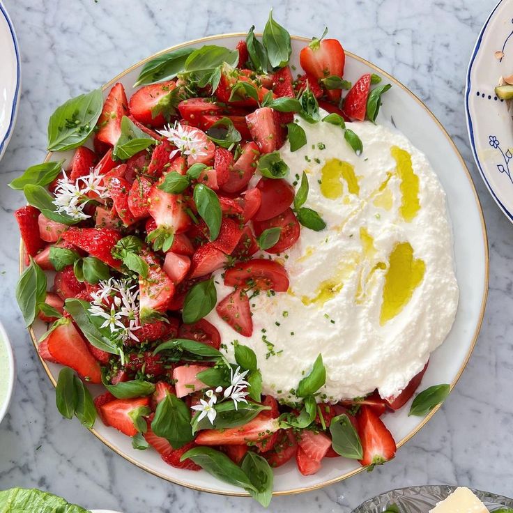 a plate with strawberries and greens on it next to other plates of salads