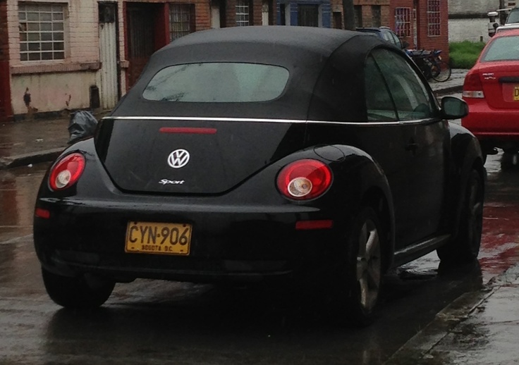 a black beetle parked on the side of a road in the rain next to some buildings