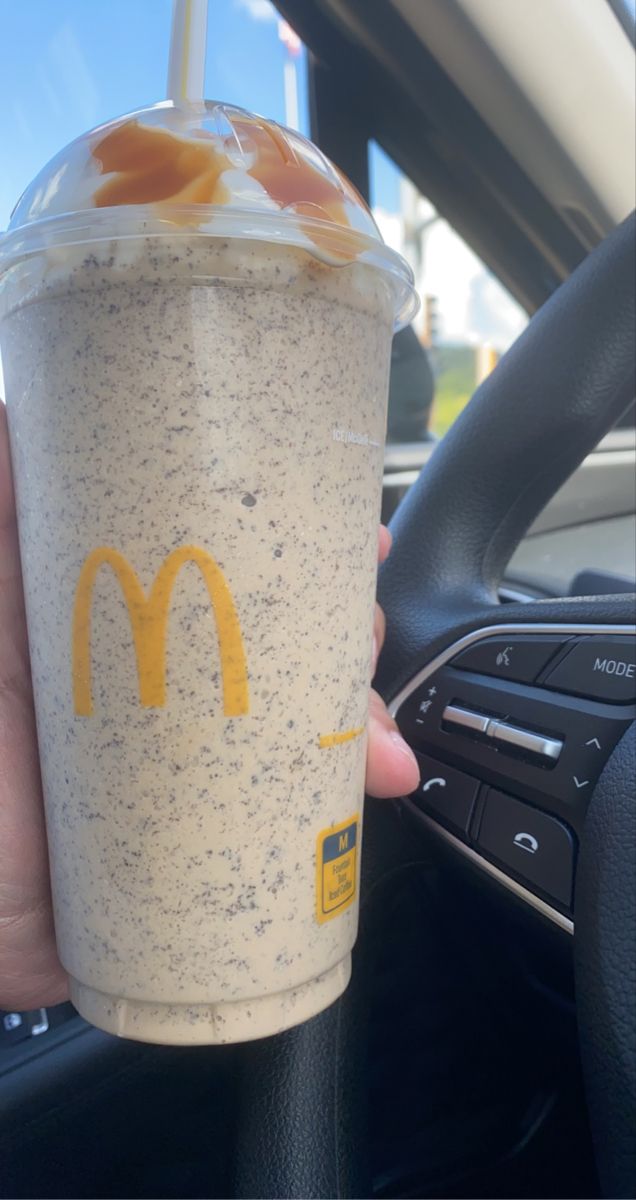 a person is holding a drink in their hand and steering wheel behind the car,