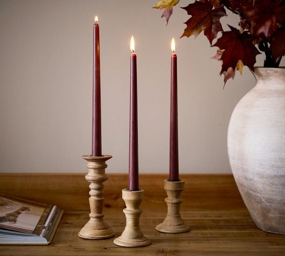 three candles are sitting on a table next to a vase with autumn leaves in it