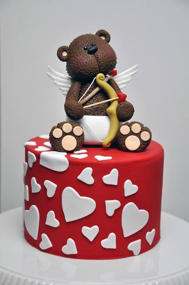 a teddy bear sitting on top of a red and white cake with hearts around it