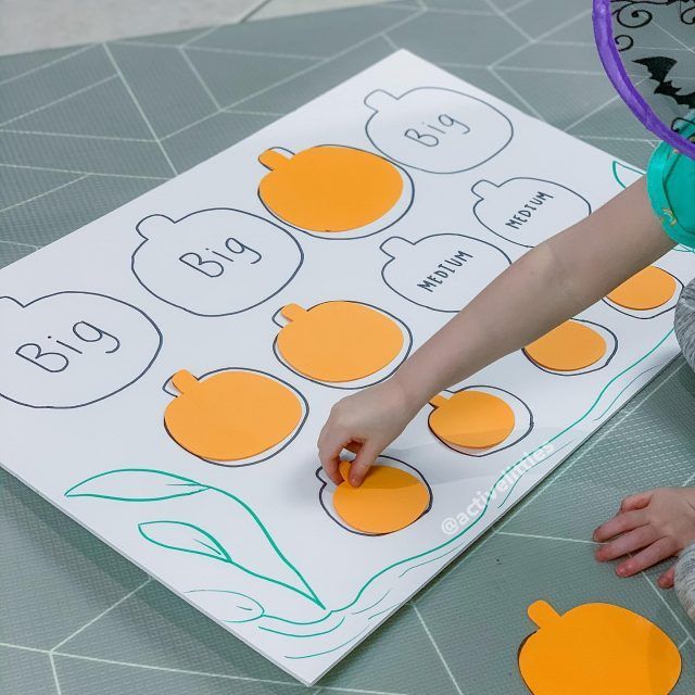 a young child is using scissors to cut out pumpkins on a sheet of paper