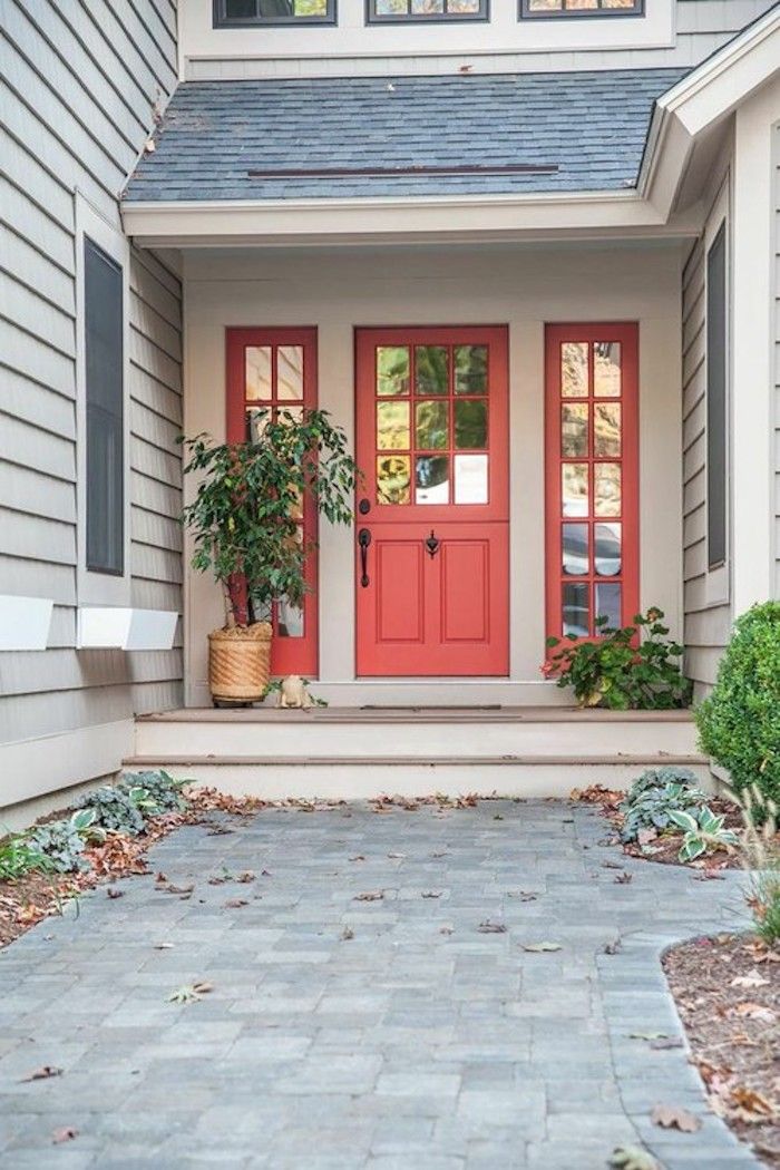 a red front door with two potted plants on the steps and a brick walkway