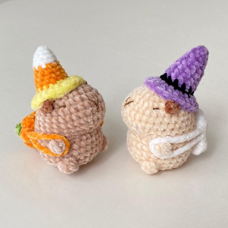 two small crocheted animals with hats on their heads are sitting next to each other