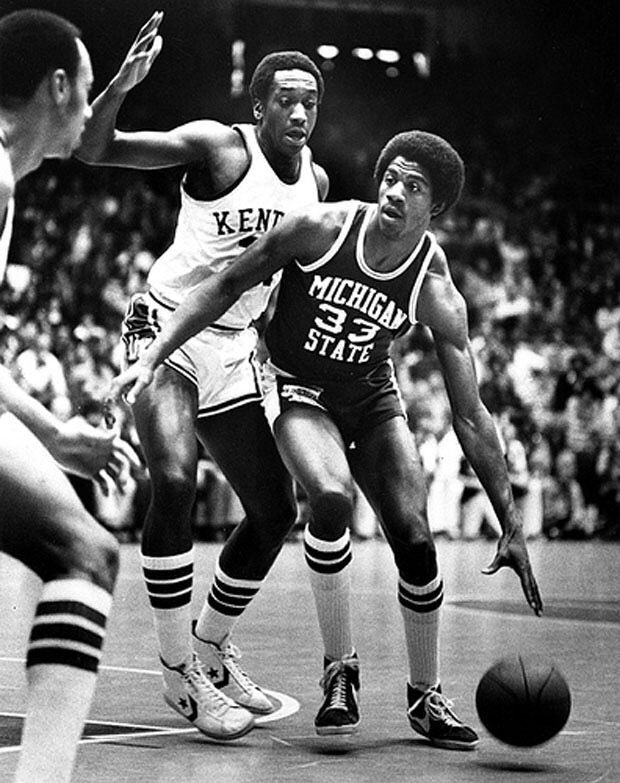 two men are playing basketball on a court with fans in the stands and one man is reaching for the ball