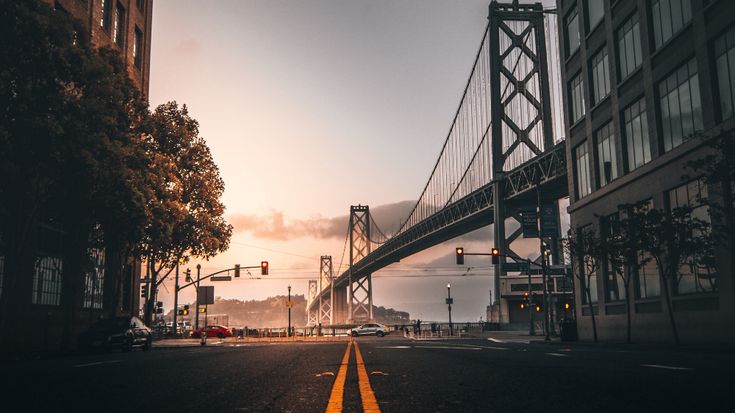 the sun is setting on an empty street in front of some tall buildings and a bridge