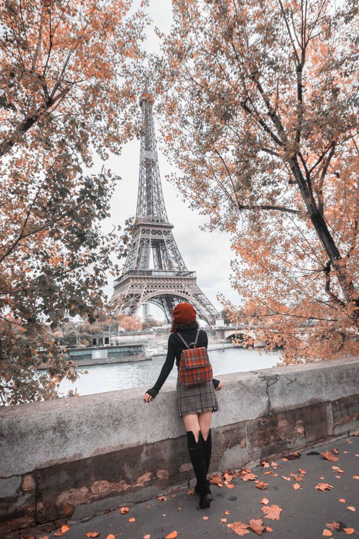 a woman standing in front of the eiffel tower with autumn leaves on the ground